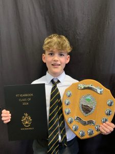 Young student holding award and certificate celebrating academic success at Inchmarlo School.