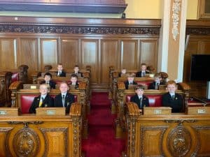 Group of students sitting in a historic assembly hall with wooden paneling and ornate furniture.