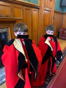 Two young children dressed in red ceremonial robes standing in a formal setting.
