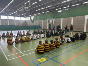 Indoor sports hall with children seated on the court, engaging in activities.