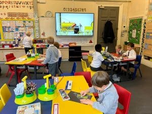 Students working on classroom activities with colorful supplies and educational posters in the background.