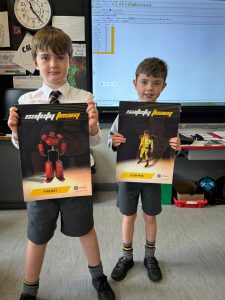 Two young boys holding books in classroom with a computer screen in the background.