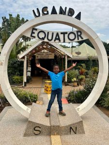 Boy standing at Equator sign in Uganda, Africa, exploring equator facts and scenery.