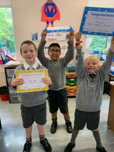 Three happy students holding certificates and awards in a classroom.