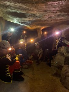 Group exploring an ancient cave with torchlights in a subterranean setting.