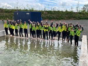 Group of people wearing high-visibility vests standing in the water at Inchmarlo, celebrating and enjoying outdoor team activities.
