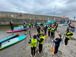 Children and instructors prepare for paddleboarding at Inchmarlo Beach, a scenic seaside location.