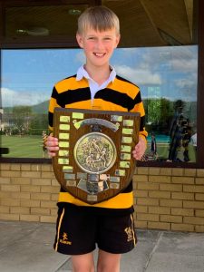 Smiling boy holding a detailed trophy outside with a grassy field in the background.