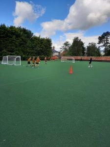 Wide view of children playing soccer at Inchmarlo sports field under bright sky.