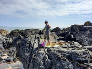 Person exploring rocky coast in Scotland with scenic ocean view.