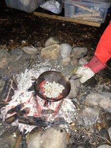 Outdoor cooking over fire with skillet on stones, rustic setting.