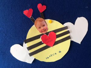 Colorful paper craft of a bee with a smiling child's face on a blue background.