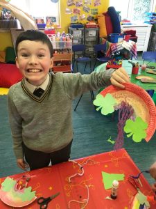 Child holding colorful rainbow craft at Inchmarlo preschool.