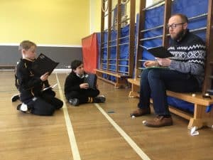 Children reading with teacher at Inchmarlo School sports hall.
