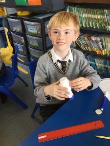 Young boy smiling in classroom with school supplies and books.