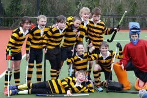 Group of young children in black and yellow striped hockey uniforms on the field with coach.