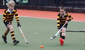 Young boys playing hockey on the field in sports uniforms.