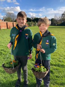 Two Boy Scouts with baskets of flowers outdoors at Inchmarlo; community, outdoor activities, youth programs.