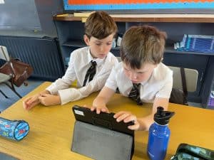 Two boys engaging with a tablet in a classroom setting at Inchmarlo, showcasing modern education.