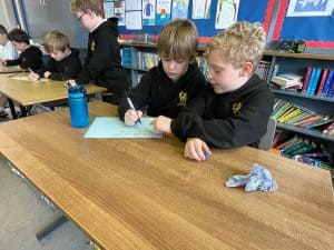 Two young students working together at a school desk in a library setting.