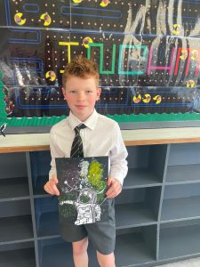 Young boy holding colorful artwork school project in classroom.