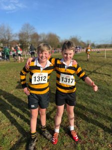 Two young boys smiling at a cross-country race, wearing striped sports jerseys.