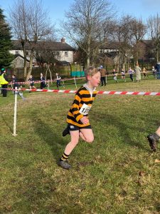 Young boy running in outdoor race at Inchmarlo estate, lush green field, trees, and residential area in background.