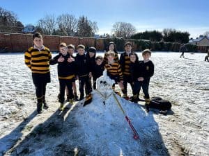 Group of children in school uniforms posing next to a snowman outdoors during winter at Inchmarlo.