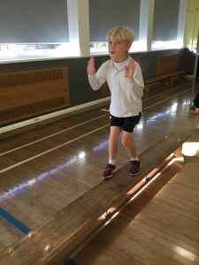 A young child balancing on a wooden beam during a sports activity at Inchmarlo school.