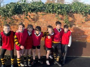 Group of schoolchildren in sports uniforms outdoors, standing against a brick wall.