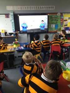 Students watching an educational video on a smart board in a lively classroom setting.