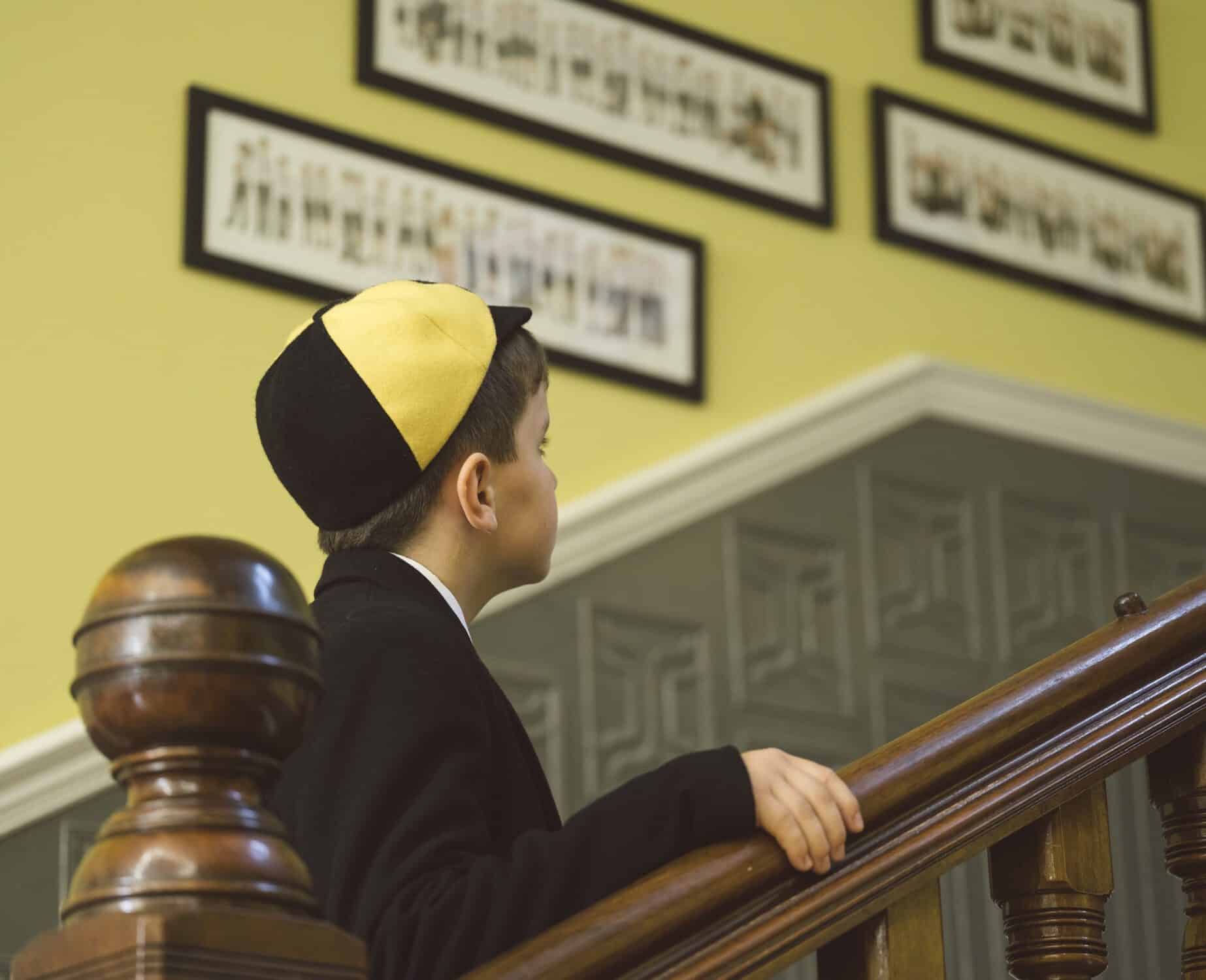 Boy in traditional Jewish attire reading and praying on synagogue stairs.