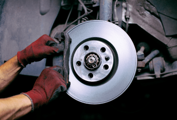 Technician inspecting a car's brake disc during maintenance at Inspired Automotive.