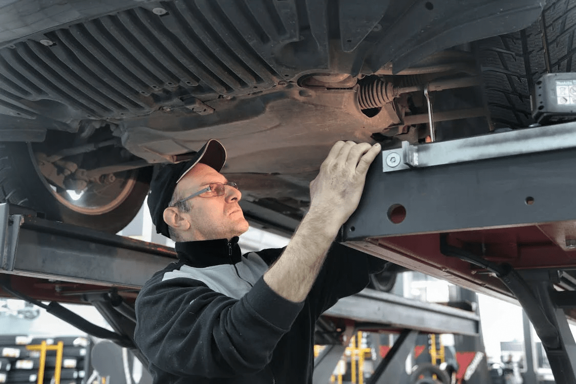 Auto mechanic inspecting vehicle under car lift in repair shop.