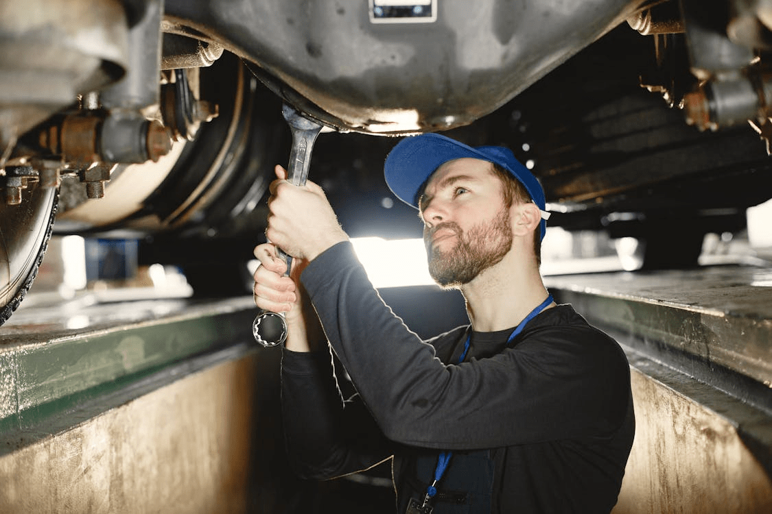 Auto repair technician inspecting under vehicle in garage.