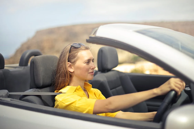 Woman driving convertible car on scenic road, promoting eco-friendly driving habits.