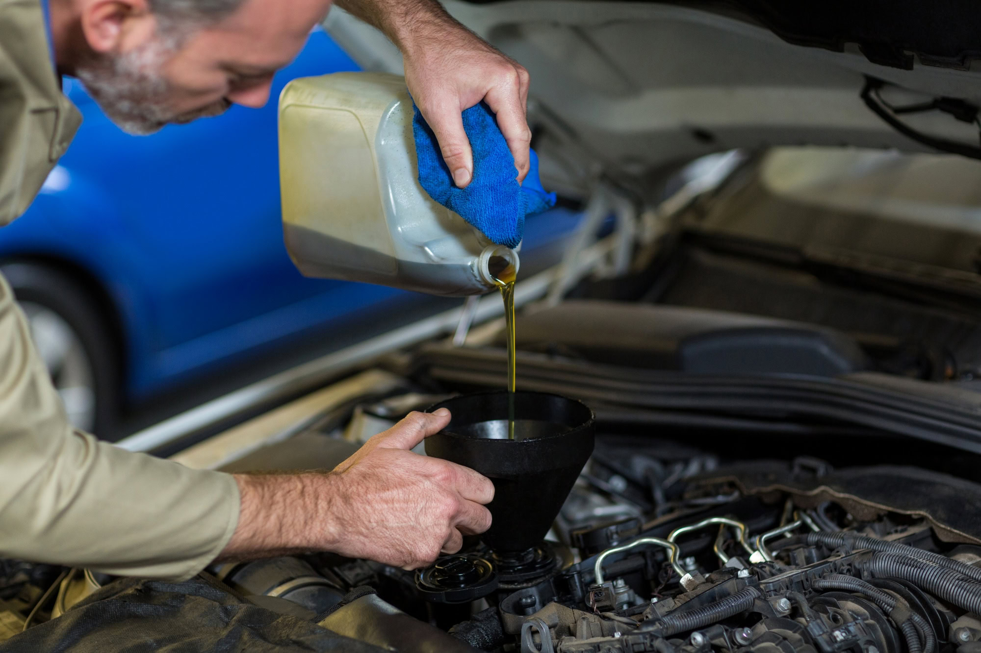 Man pouring engine oil during a regular oil change service at an automotive shop.