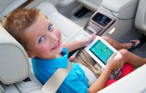 Child with blue eyes using a tablet in a car seat.