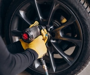 Technician inspecting car tire with air pressure gauge during service.