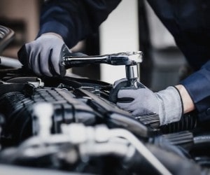 Auto repair technician inspecting and repairing a car engine with tools.