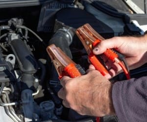 Technician testing car battery with diagnostic tools under the hood.