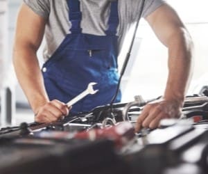 Skilled auto repair technician inspecting car engine in workshop.