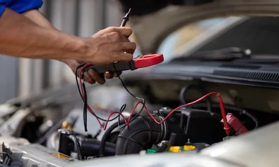 Technician testing car battery with multimeter in auto repair shop.