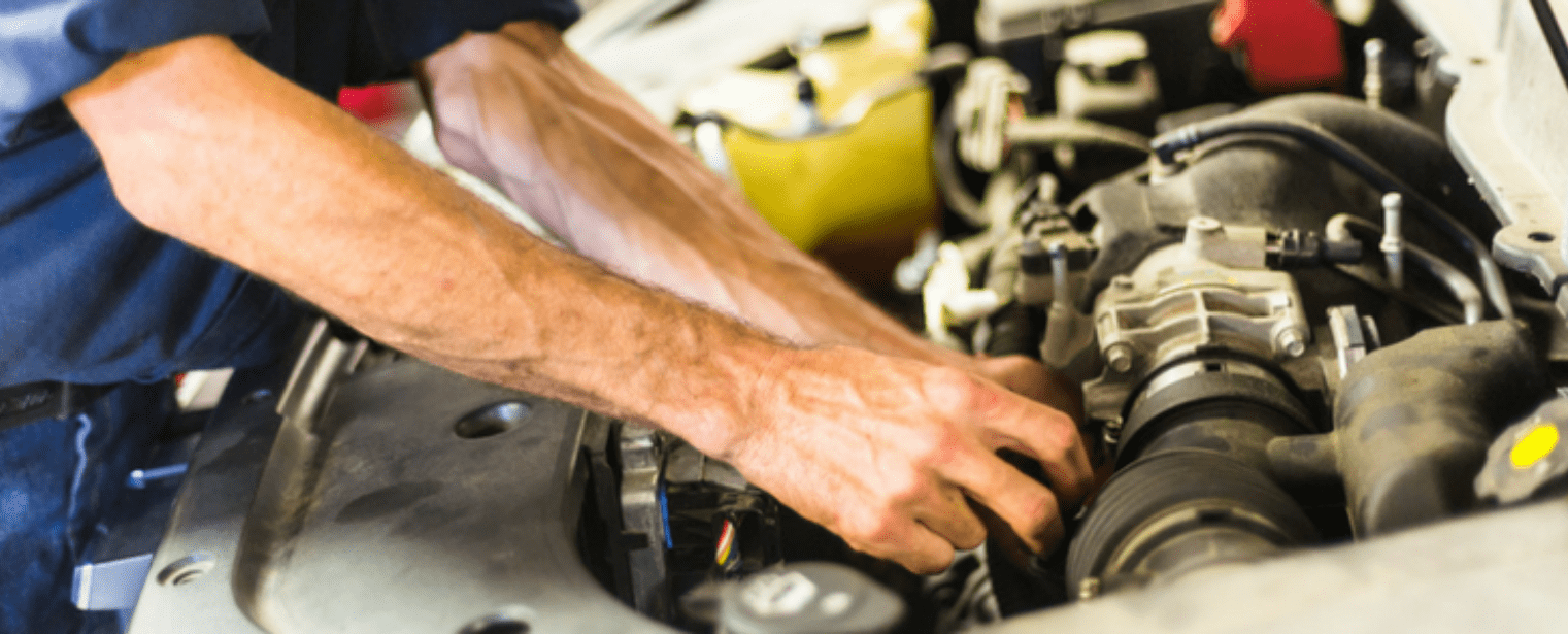 Auto repair technician inspecting car engine for maintenance or repair.