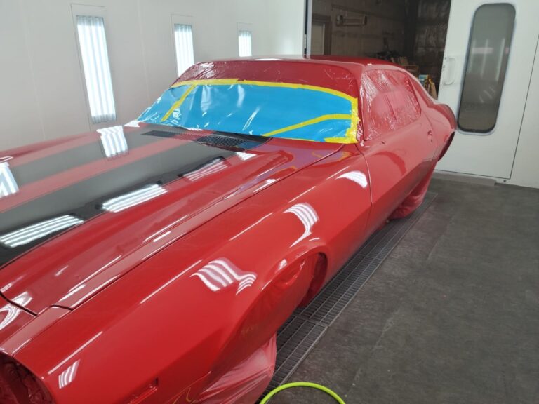 Vintage red muscle car being restored in a professional auto body shop.