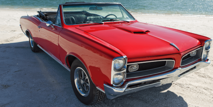 Restored vintage convertible car on the beach, showcasing expert automotive restoration services.