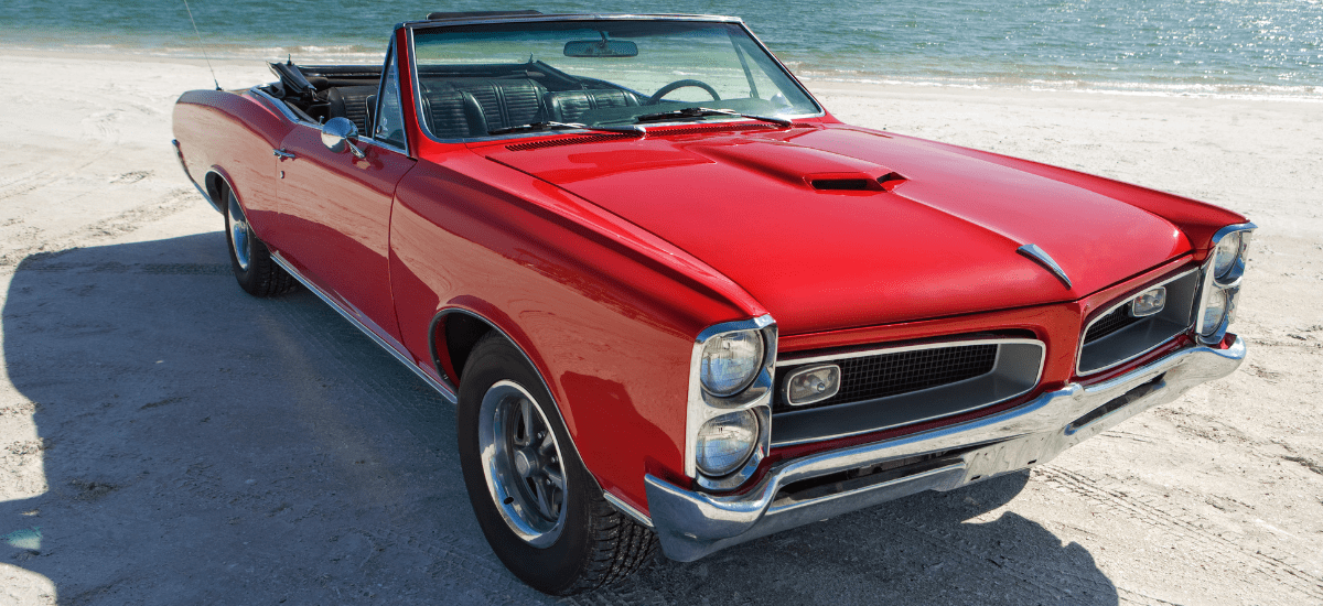 Restored vintage convertible car on the beach, showcasing expert automotive restoration services.