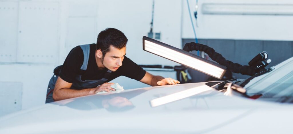 Automotive body repair technician examining a car's exterior for damage or imperfections.