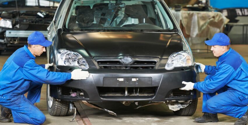 Automotive body repair technicians working on a black car in a repair shop.
