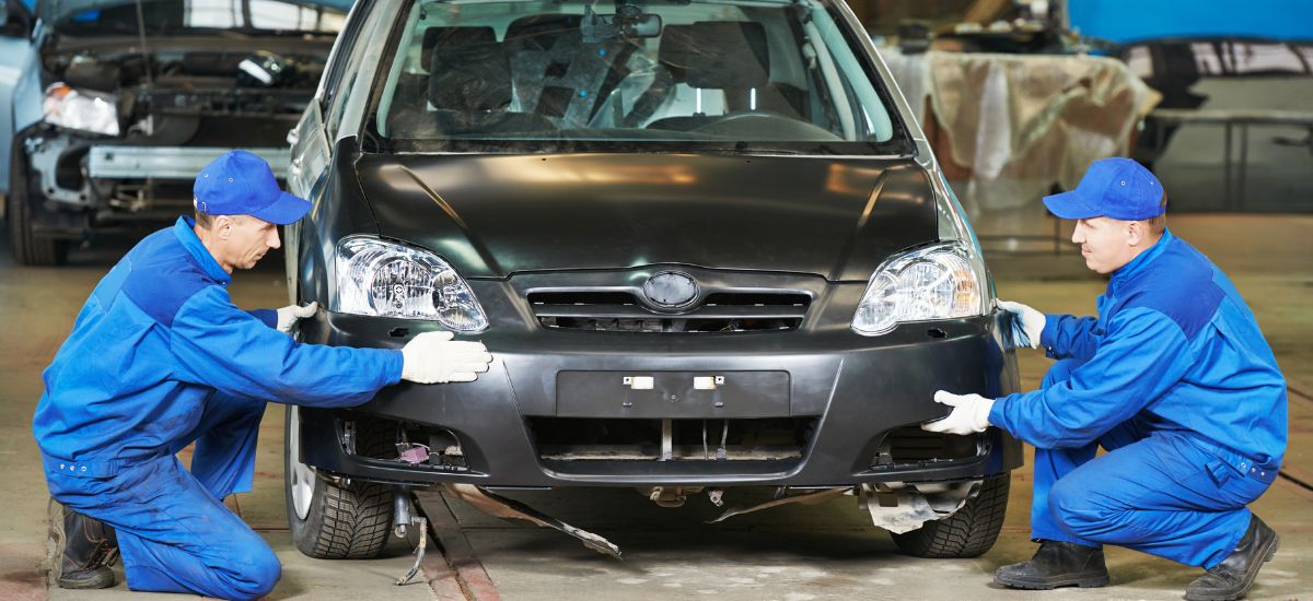 Automotive body repair technicians working on a black car in a repair shop.